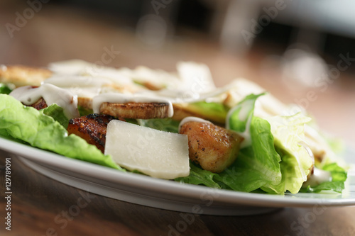 closeup shot of caesar salad with chicken on old wooden table, shallow focus