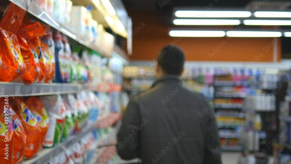 Young man choosing household chemicals in supermarket. Handsome guy selects fabric softener or washing powder at the store and put it a shopping cart. Department of cleaning product and home care Young man choosing household chemicals in supermarket. Handsome guy selects fabric softener or washing powder at the store and put it a shopping cart. Department of cleaning product and home care