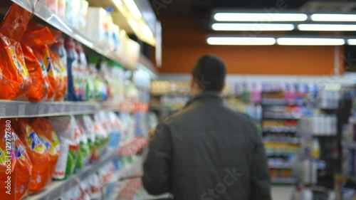 Wallpaper Mural Young man choosing household chemicals in supermarket. Handsome guy selects fabric softener or washing powder at the store and put it a shopping cart. Department of cleaning product and home care Torontodigital.ca