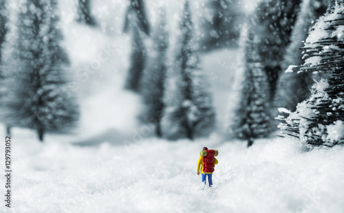 Miniature backpacker walking in pine forest during winter
