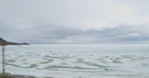 Wide scenic pan of frozen bay to sheer mountains on cloudy day photo