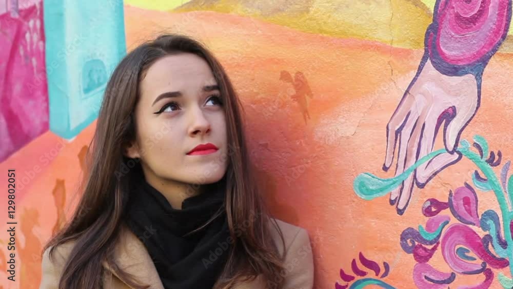 Cute young woman look to you by standing, near the vibrant wall. Cute young woman look to you by standing, near the vibrant wall.