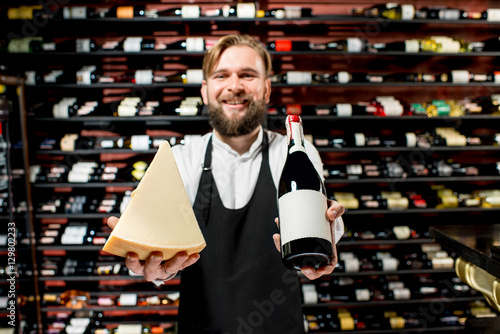 Portrait of a sommelier in uniform with parmegiano cheese and bottle of wine at the restaurant or supermarket. Choosing wine according to the type of cheese. Bottle with empty label to copy paste photo