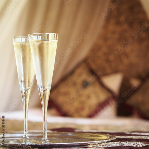 Two champagne glasses with oriental canopy bed at the background