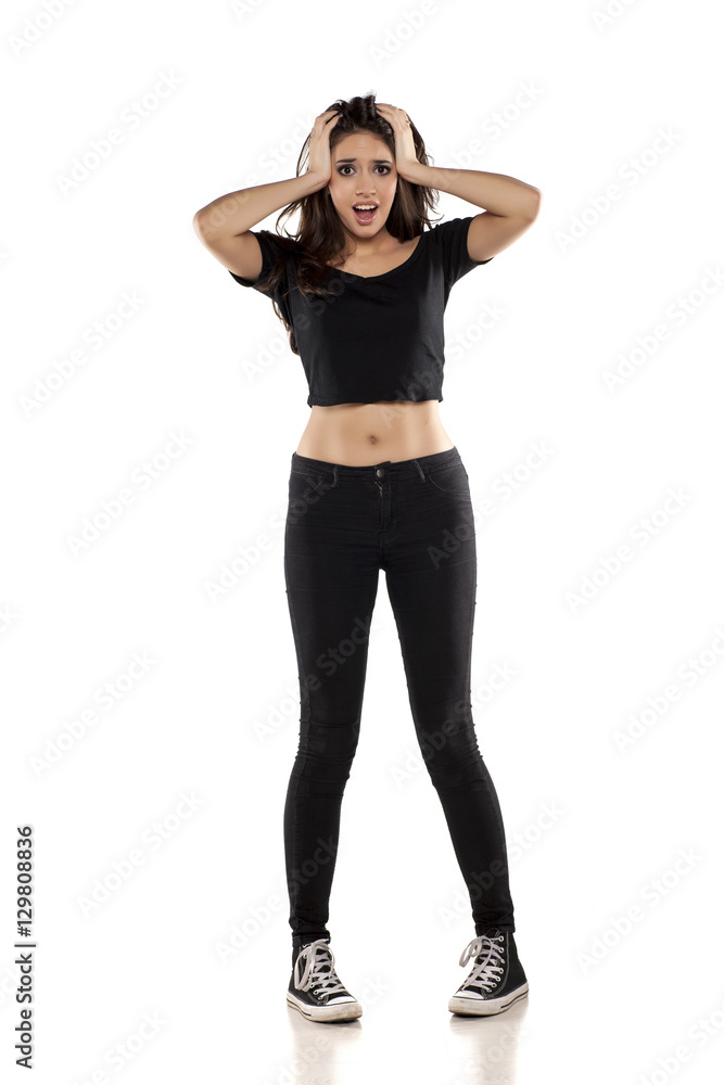 shocked young woman in black pants, shirt and sneakers on a white background shocked young woman in black pants, shirt and sneakers on a white background