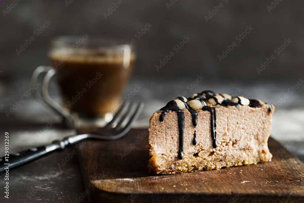 Slice of raw chocolate mousse cake with cashew, hazelnuts and dark chocolate glaze topping and coffee on a wooden and grey background. Vegan sugar, gluten free dessert. Copy space Slice of raw chocolate mousse cake with cashew, hazelnuts and dark chocolate glaze topping and coffee on a wooden and grey background. Vegan sugar, gluten free dessert. Copy space