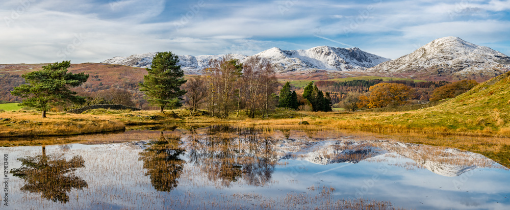 Fototapeta premium Cumbrian snowcapped mountains with clear reflections in Kelly Hall Tarn on a Autumnal afternoon.
