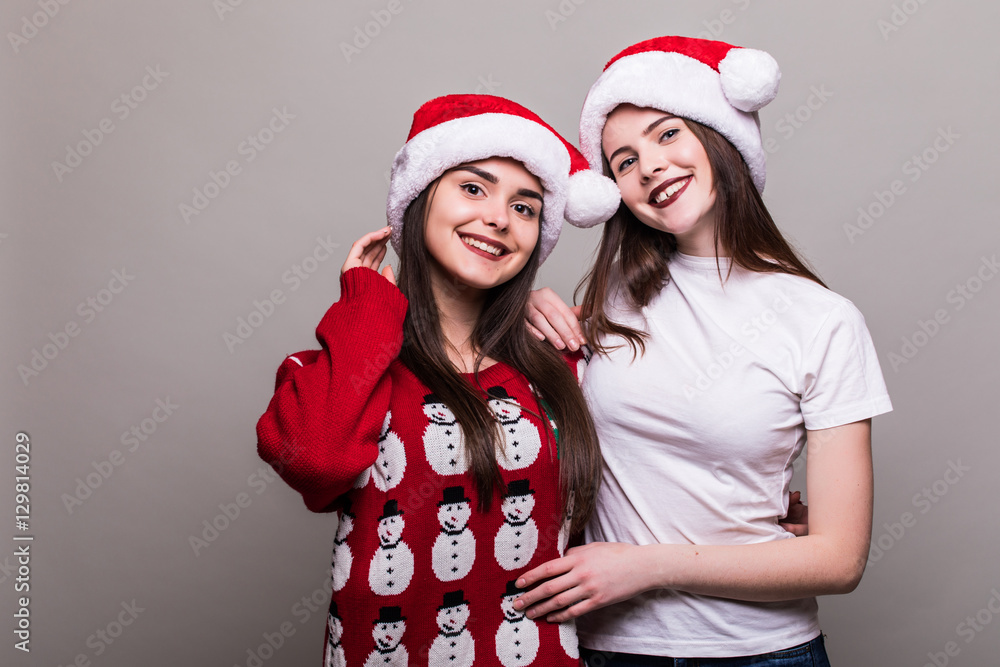Two girls in Santa hat isolated on grey background Two girls in Santa hat isolated on grey background