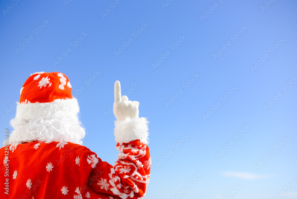 Santa Claus pointing finger up light blue background. Back view