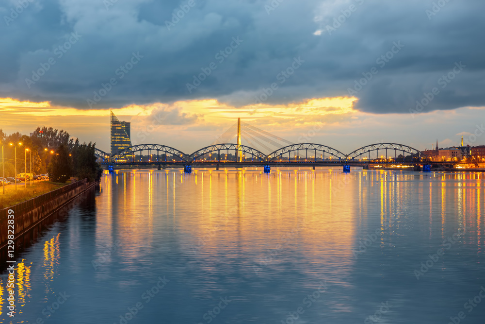 Naklejka premium Night view on the illuminated bridge with reflection on the water in Riga, Latvia. Wide angle view with copy space