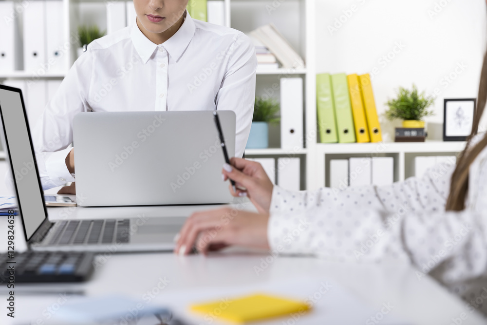 Woman typing while her colleague is chilling out with a pen Woman typing while her colleague is chilling out with a pen