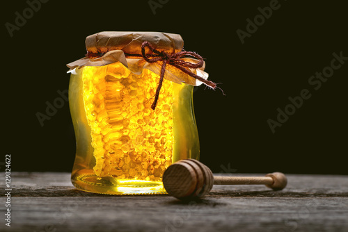 jar of honey with honeycomb with wooden dipper on wooden table photo