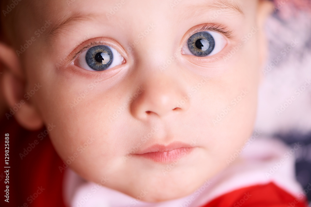 Close up of a beautiful baby boy's face with glowing blue eyes looking straight into the camera with a calm expression Close up of a beautiful baby boy's face with glowing blue eyes looking straight into the camera with a calm expression