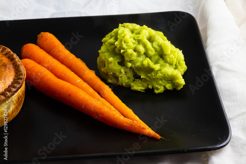 Savoury pie served with glazed carrots and mushy peas.