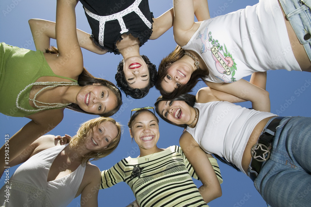 Directly below shot of cheerful female friends forming huddle against blue sky