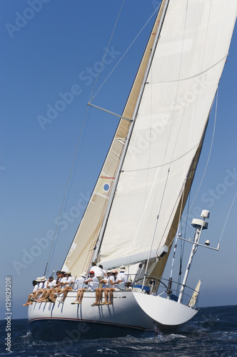 Stampa su tela Group of crew members sitting on the side of a sailboat in the ocean