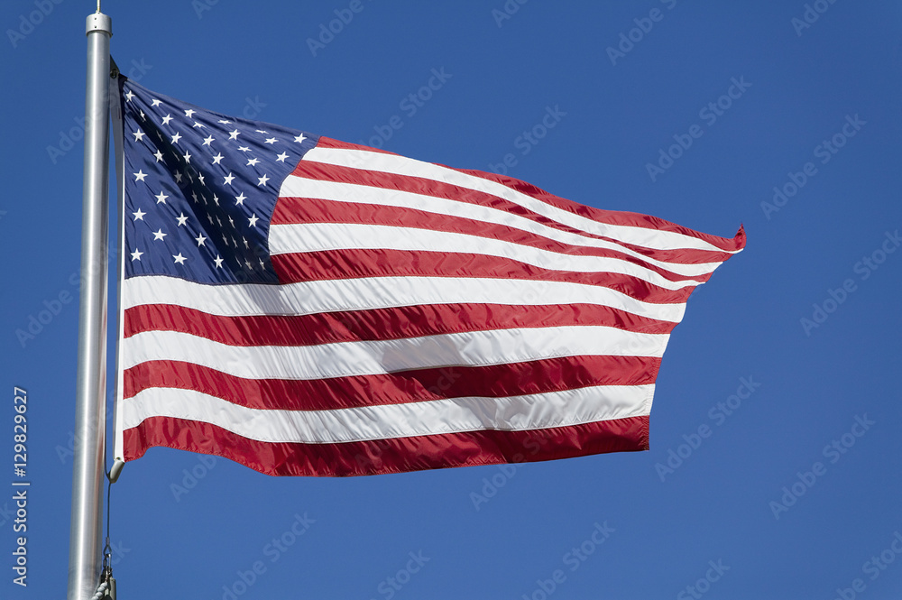 Fototapeta premium American flag waves in the wind against a blue sky
