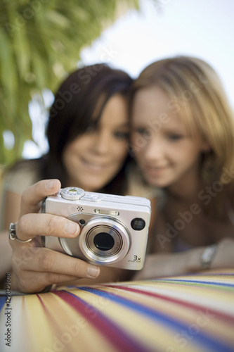 Two young women looking at pictures on digital camera in backyard focus on camera ground view