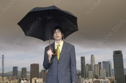 Young businessman holding umbrella with cityscape in the background