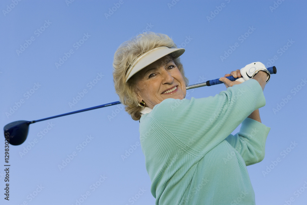 Portrait of a happy senior woman swinging a golf club against clear sky Portrait of a happy senior woman swinging a golf club against clear sky