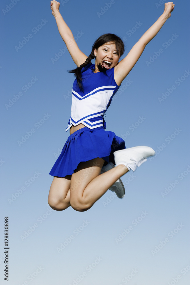 Full length of an excited young cheerleader jumping against sky Full length of an excited young cheerleader jumping against sky