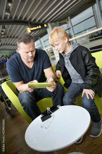 Germany, Hamburg, Mature man and boy (8-9) sitting at airport hall and using tablet photo