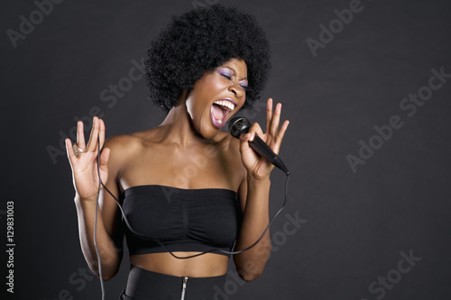 Obraz na plátně Woman singing on microphone over colored background