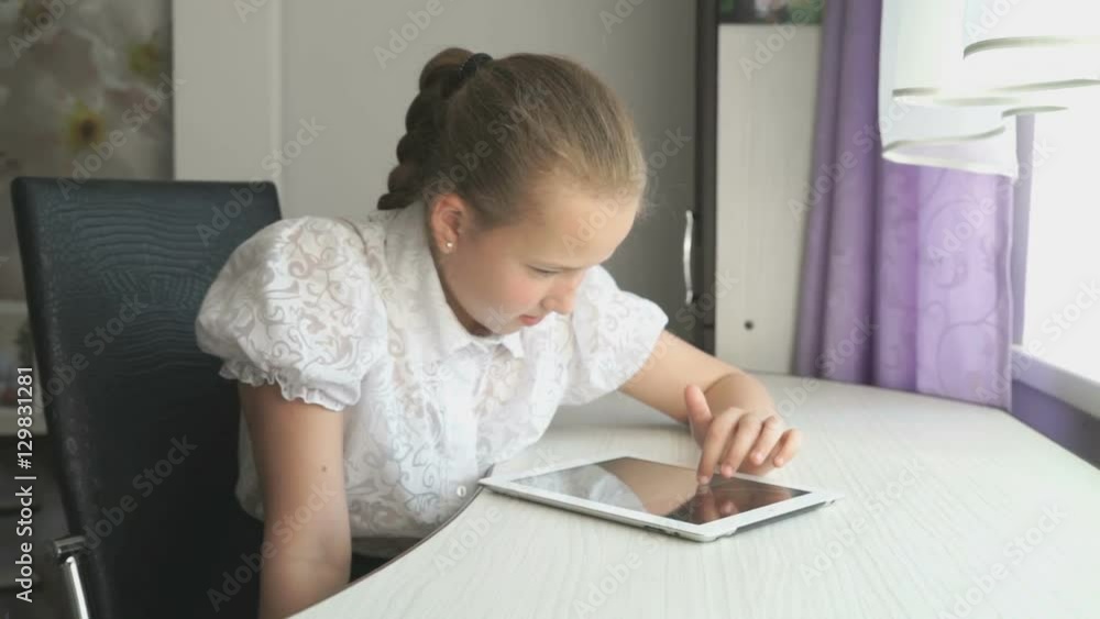 Teenager girl smiles while uses a digital tablet computer at the desk at home Teenager girl smiles while uses a digital tablet computer at the desk at home