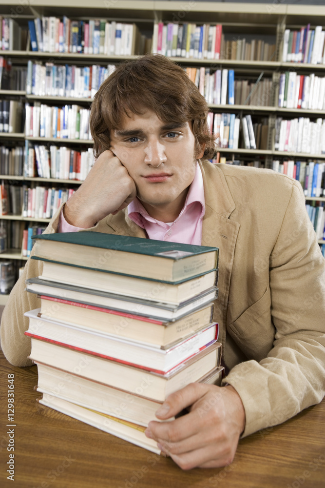Portrait of a bored college student at desk with stack of books at library Portrait of a bored college student at desk with stack of books at library