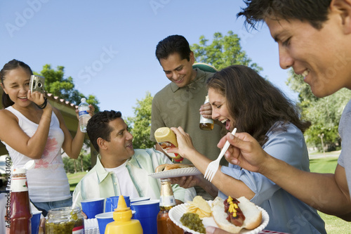 Happy family enjoying food while woman photographing them at park photo