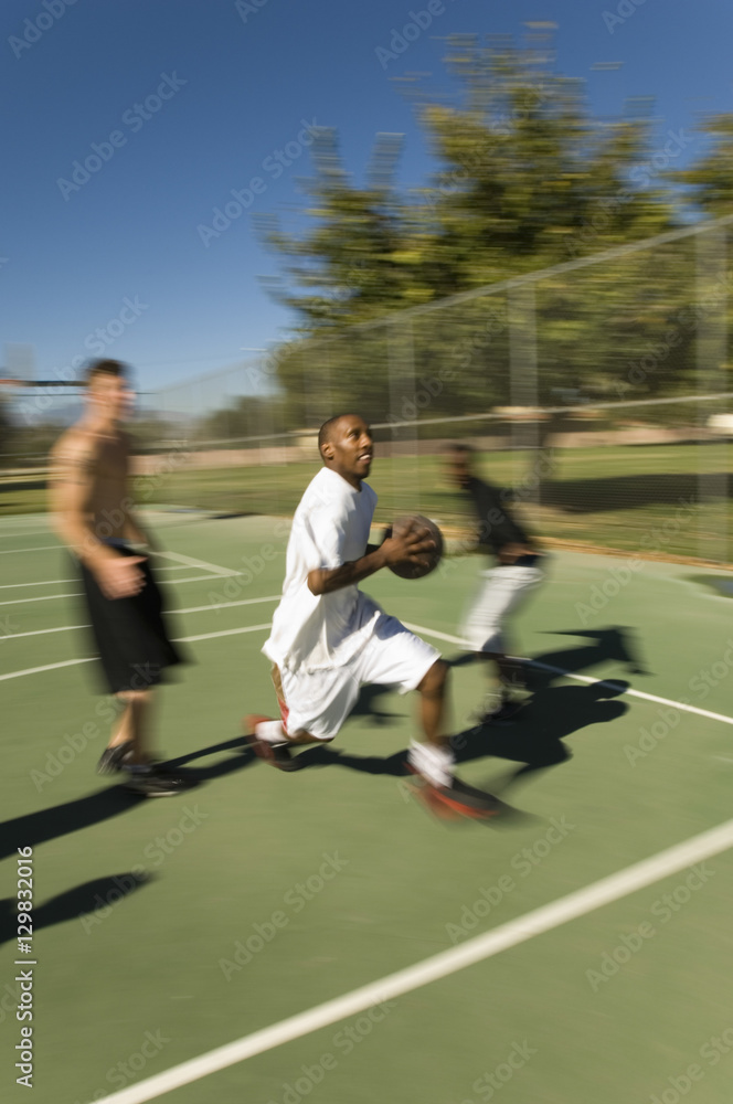 Obraz premium Full length of young male friends playing basketball on court