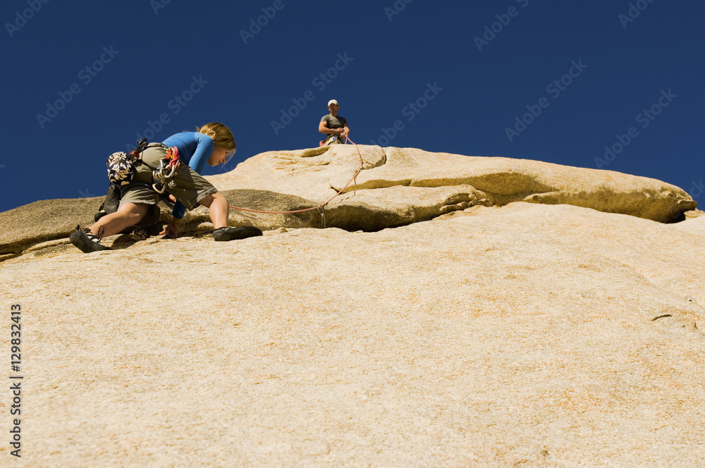 Low angle view of man assisting friend climbing rock against clear blue sky