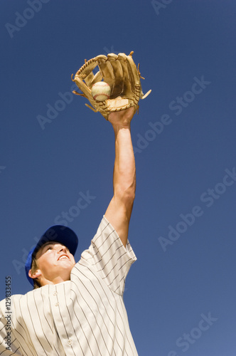 Low angle view of baseball player trying to catch the ball against blue sky