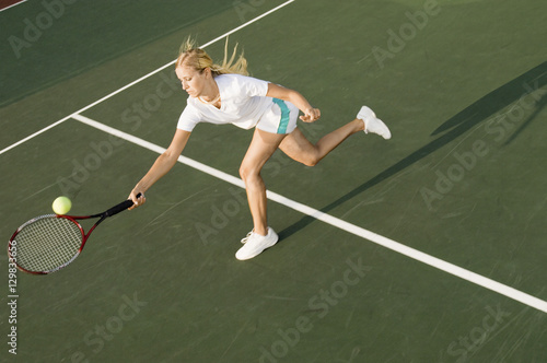 Female tennis player reaching to hit the tennis ball on court © moodboard