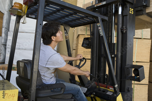 Mid adult warehouse worker stacking wood by forklift