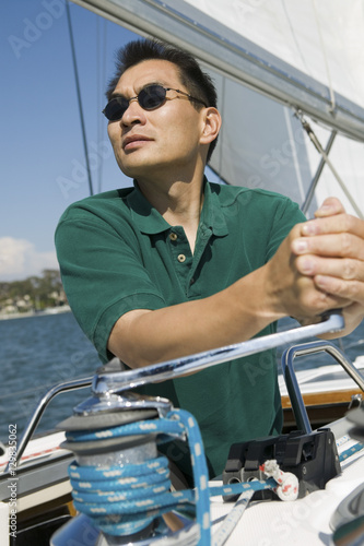 Asian man raising sail on the sailboat against clear sky © moodboard