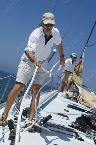 Sailors working ropes on deck of a yacht against clear blue sky and sea