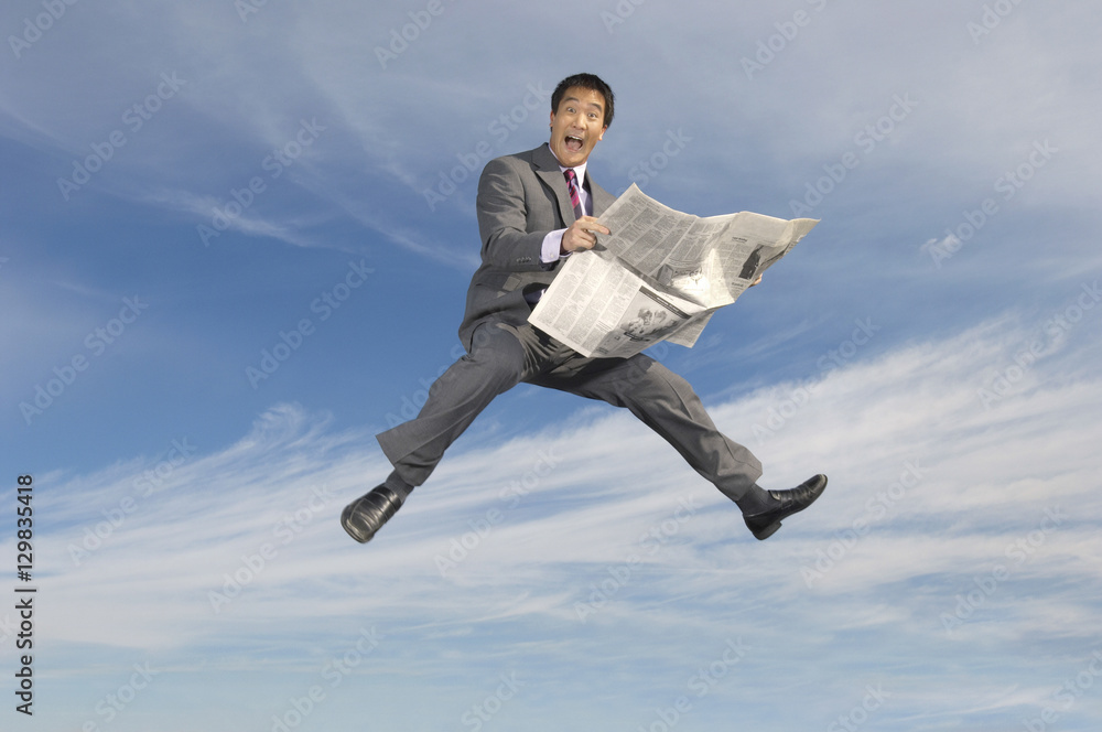 Portrait of excited young Asian businessman holding newspaper against cloudy sky