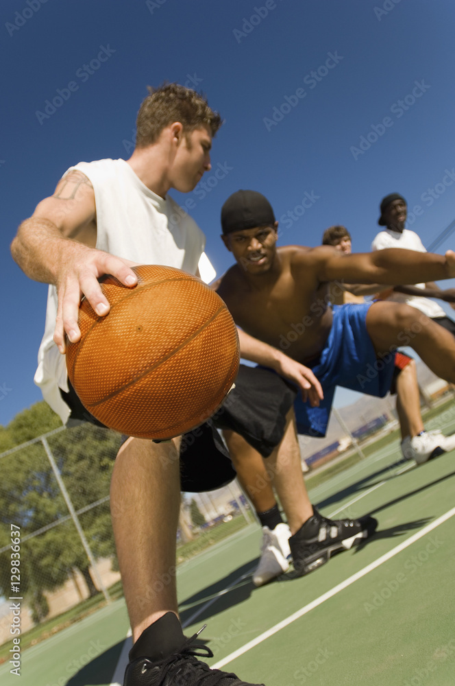 Low angle view of young men playing basketball on court Low angle view of young men playing basketball on court