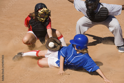 Softball player sliding into home plate while umpire rules safe