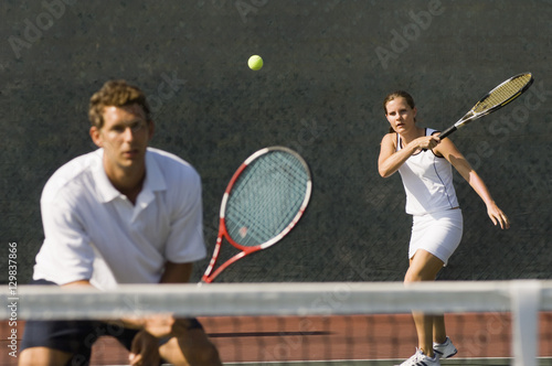 Mixed doubles player hitting tennis ball with partner standing near net © moodboard