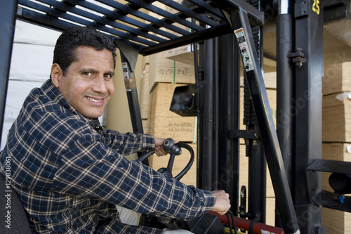 Portrait of happy mature warehouse worker driving forklift