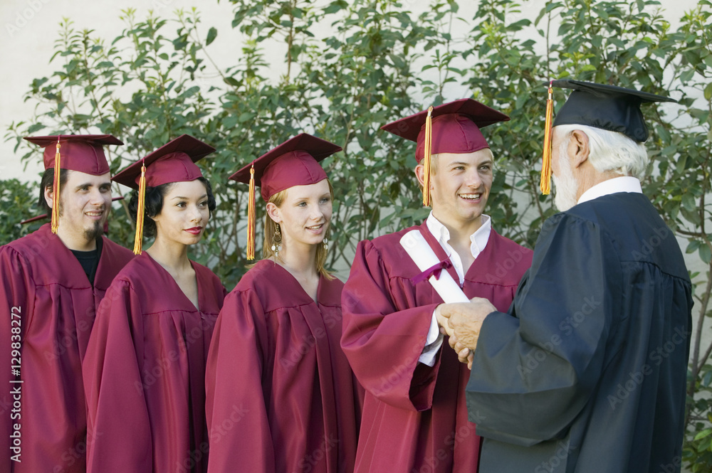 Group of graduates in line collecting certificate from male dean