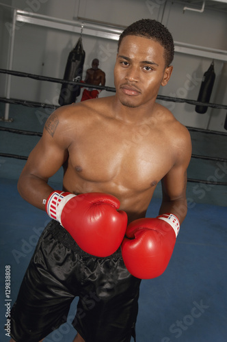 Portrait of a boxer ready for a fight in the boxing ring with competitor in the background