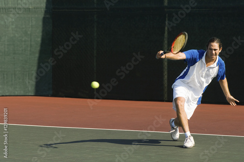 Full length of a male tennis player hitting backhand on the tennis court © moodboard