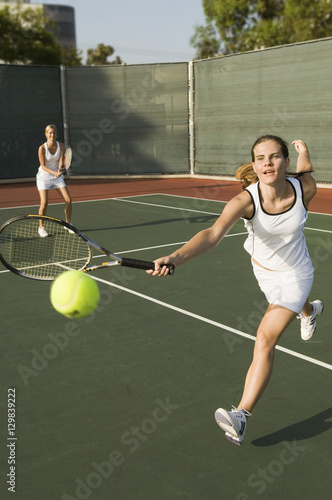 Female tennis player hitting a shot with partner standing in background © moodboard