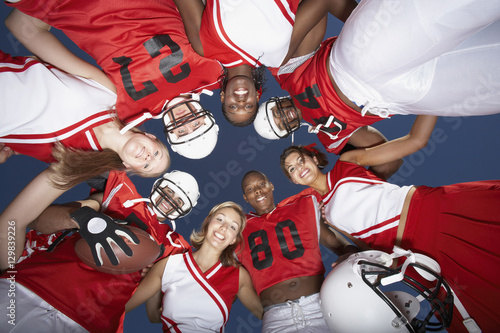 View from below of football players and cheerleaders in huddle against clear sky © moodboard