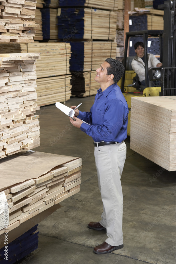 Fototapeta premium Man checking notes and laborer with forklift in the warehouse