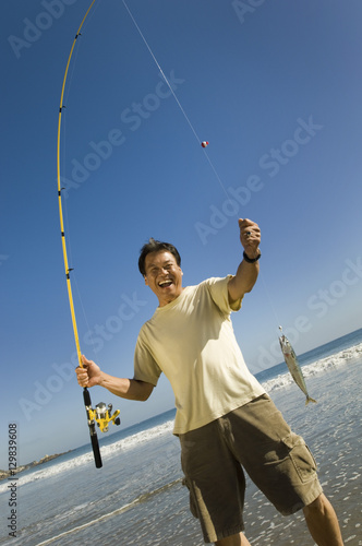 Excited man holding fishing rod and his catch on the beach