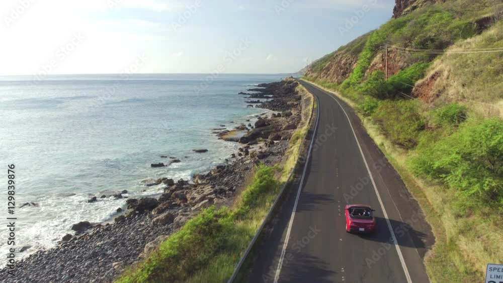 AERIAL: Red convertible car driving along coastal road above rocky shore AERIAL: Red convertible car driving along coastal road above rocky shore